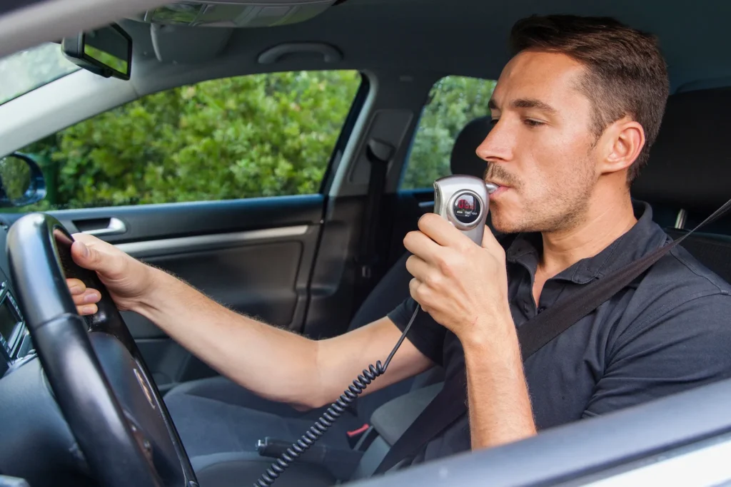 A man taking a breathalyzer test in his car.
