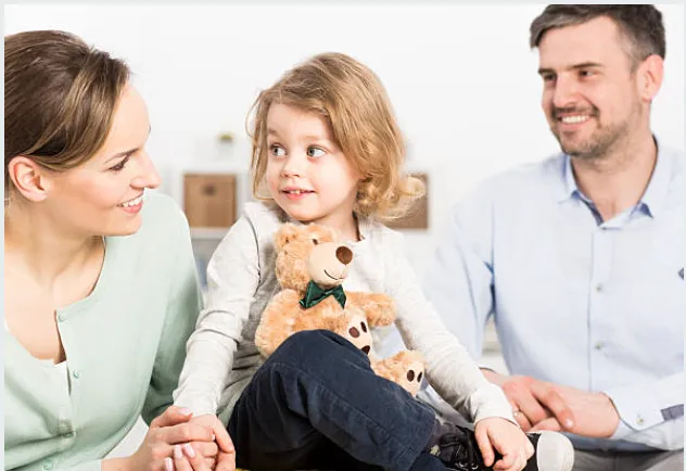 A small child sitting between her parents, with a teddy bear in her lap.