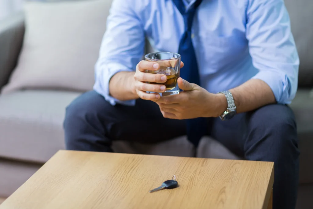 A man holding a glass of alcohol with a set of keys in front of him.