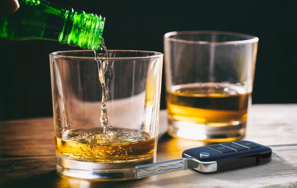 A glass of alcohol next to a set of car keys.