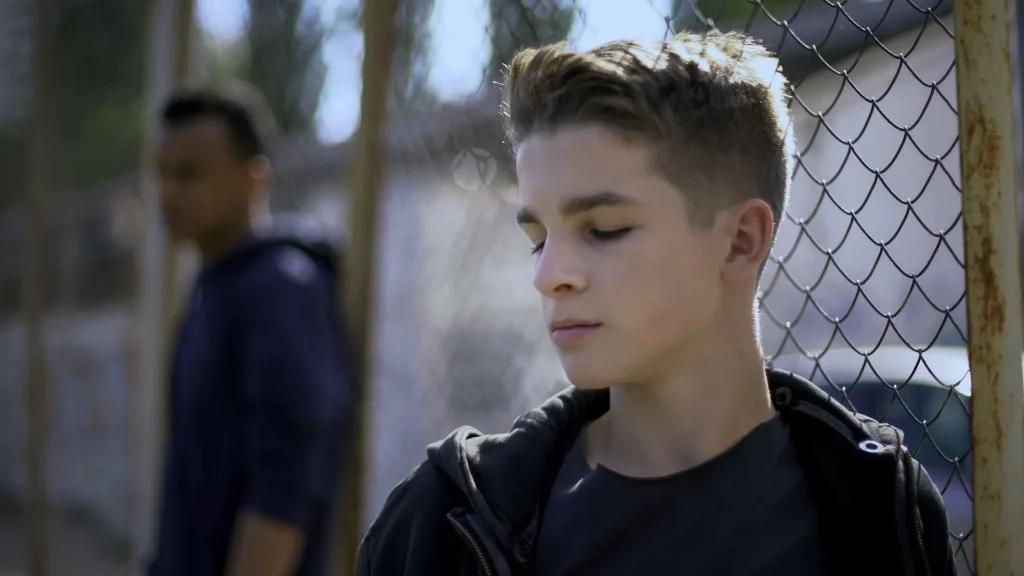 A young boy standing next to a chain-link fence.