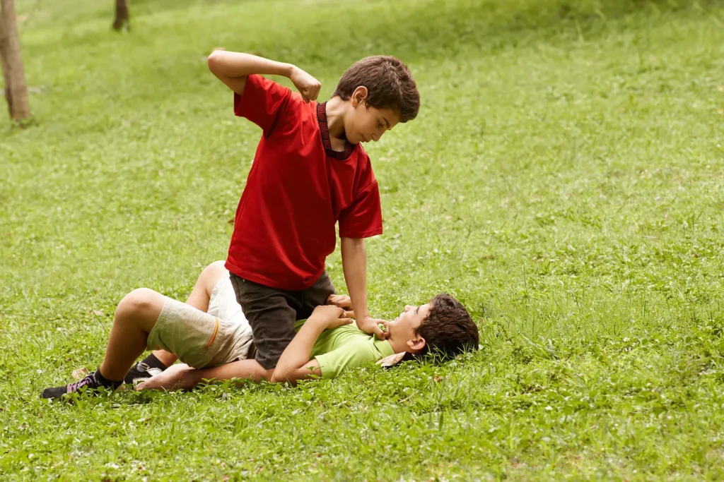 Two young boys fighting in the grass.