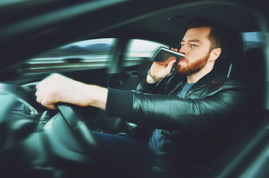 A man driving a car while drinking out of a flask.