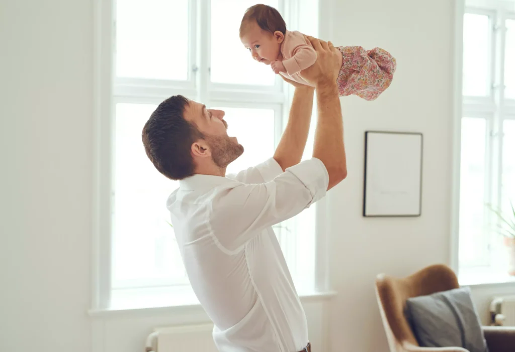 A smiling father holding his baby daughter in the air.
