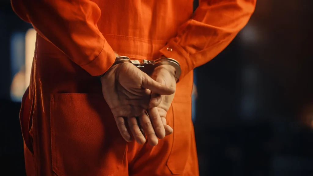 A man in an orange jumpsuit with his hands cuffed behind him.