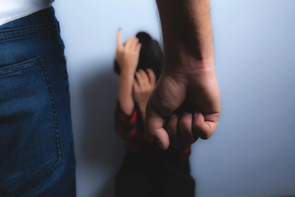 A person cowering on the floor shielding themselves as another individual raises a clenched fist in a threatening gesture.