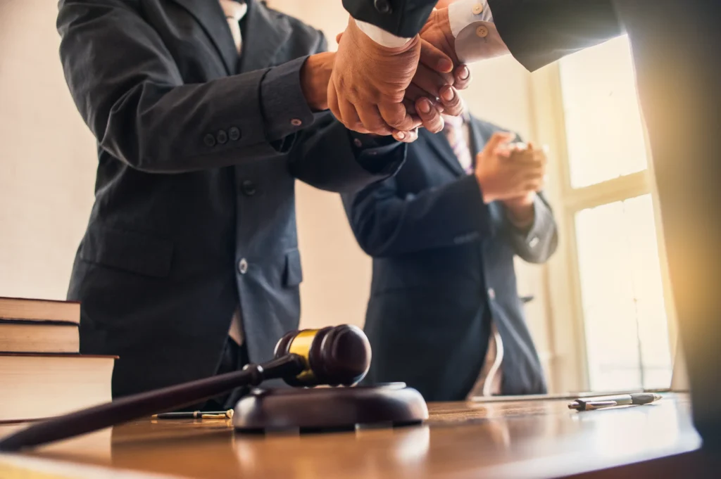 Legal professionals shaking hands in a courtroom with law books and a gavel in the foreground, symbolizing trusted representation from a Dallas domestic violence defense lawyer.
