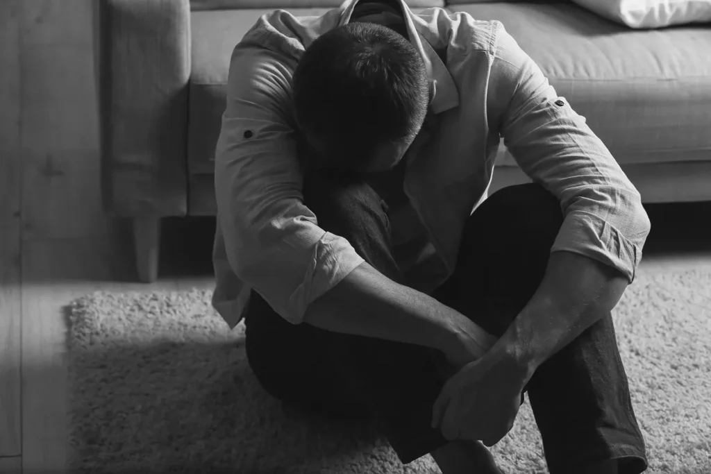 Distressed man sitting on the floor with his head down, representing the emotional impact of being charged with domestic violence in Dallas.
