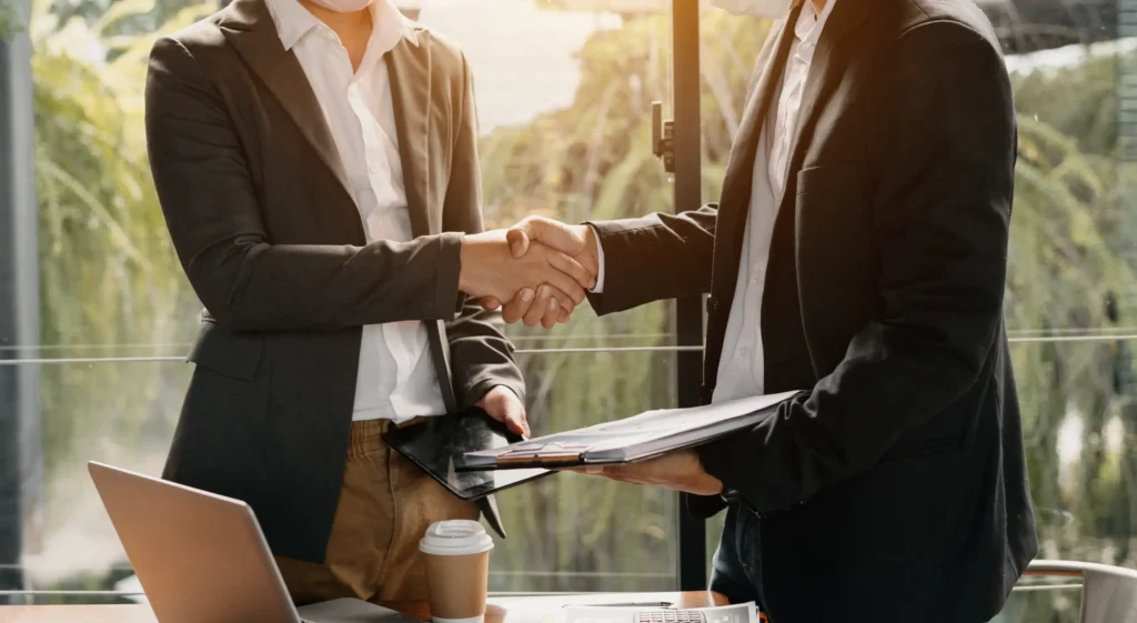 Two professionals in business attire shaking hands in a bright office, symbolizing the importance of hiring a Collin County probation violations lawyer without delay.