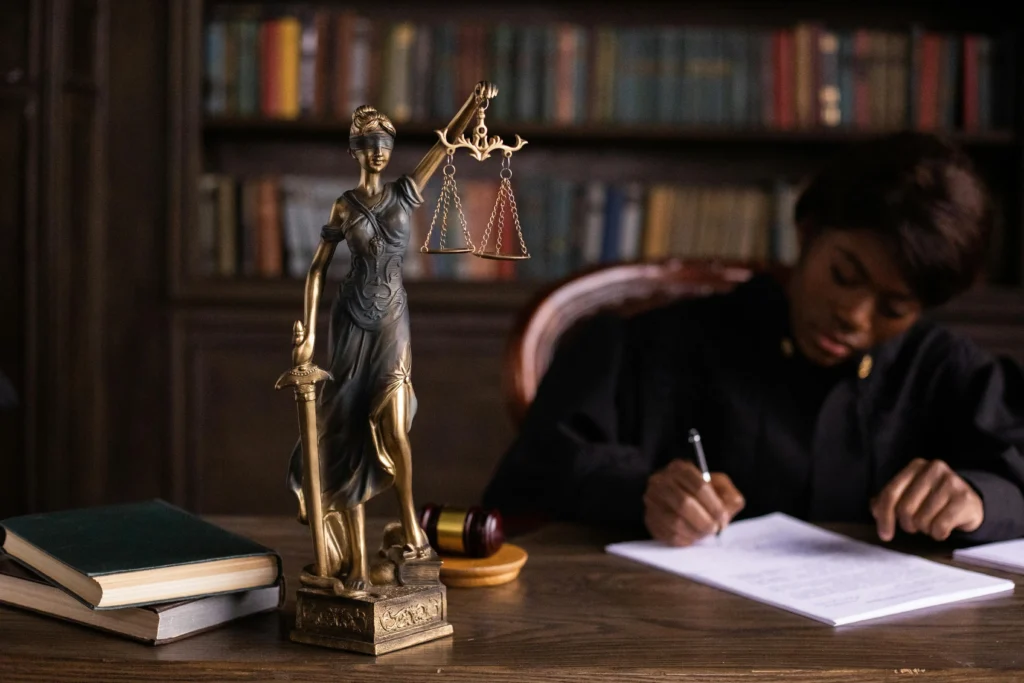 judge writing at desk with blind justice scales and gavel